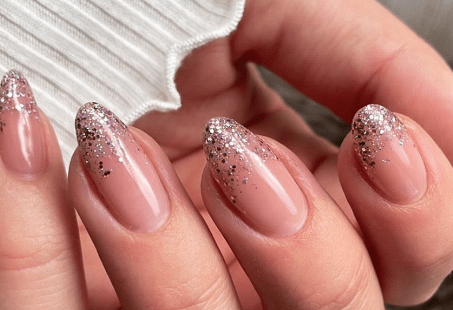 Close-up of hands with almond-shaped nails covered in pink nail polish and silver glitters.