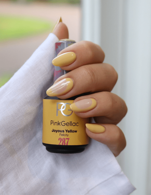 A hand with yellow painted nails is holding a bottle of nail polish labeled "Pink Gellac, Joyous Yellow, 287".