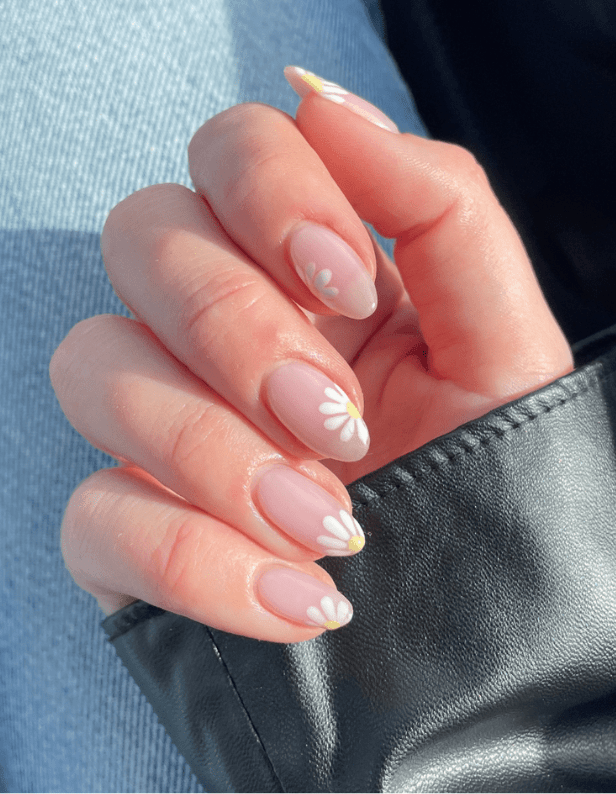 A hand with pink nail polish with white flowers on the nails, against a background of denim and a black leather jacket.