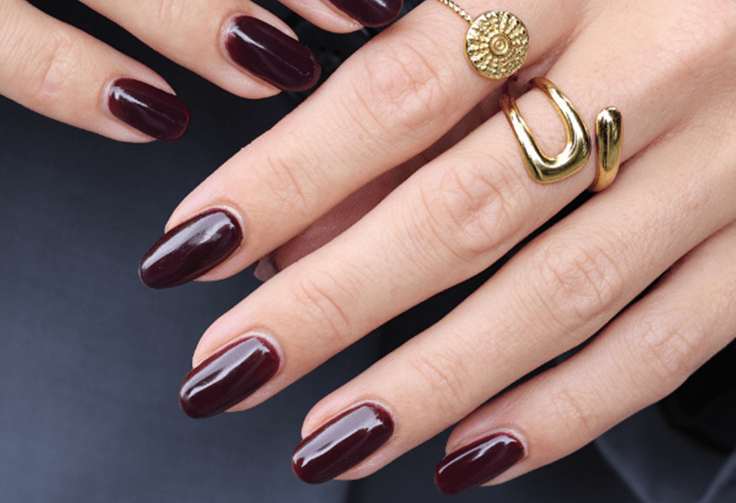 Hands with burgundy painted nails and gold rings.