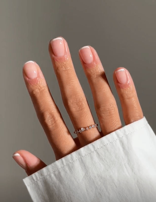 A hand with a white blouse with a ring with small stones on the ring finger and well-groomed nails with a French manicure.