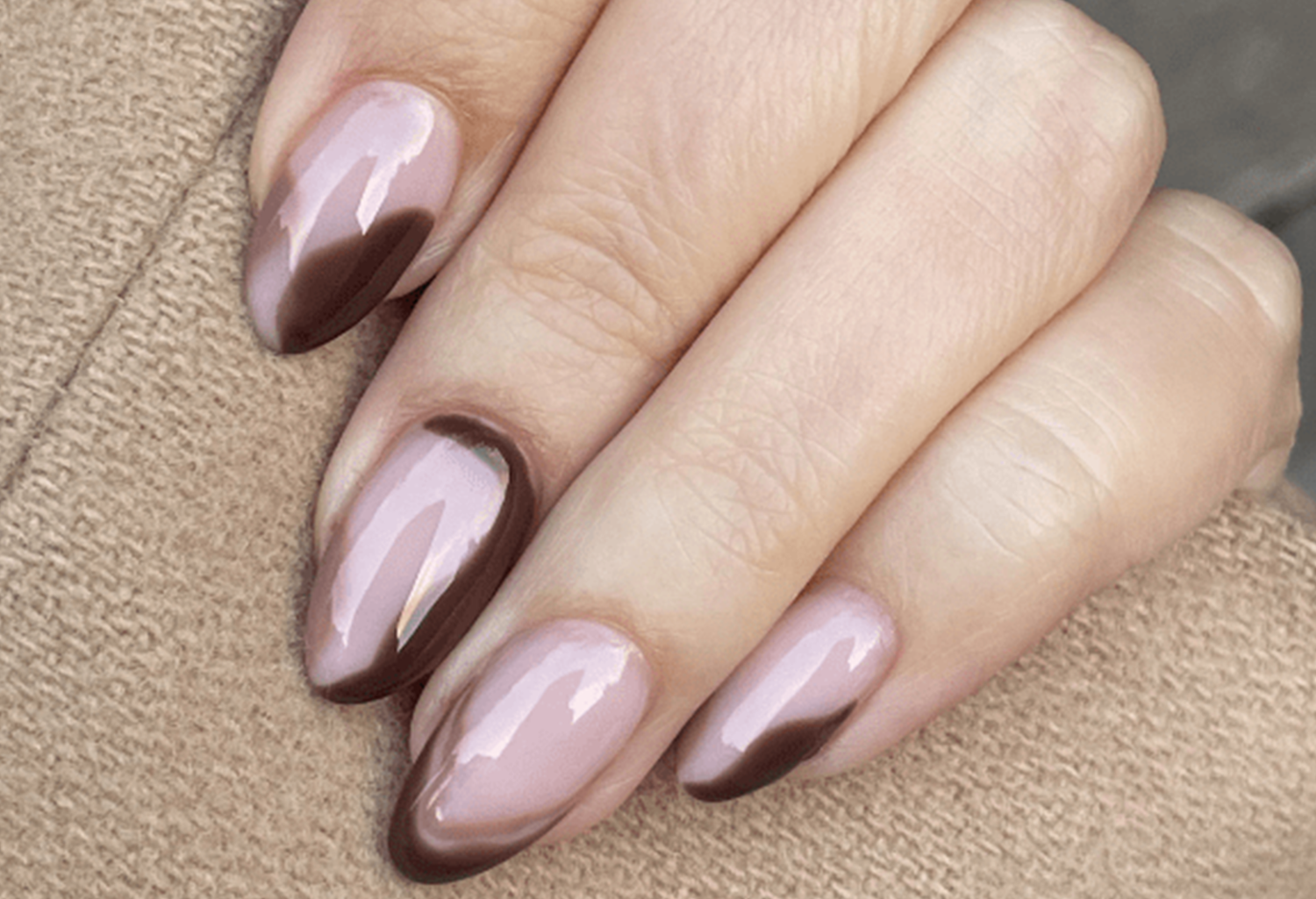 Close-up of a hand with long, almond-shaped nails with a pink and brown nail art design.