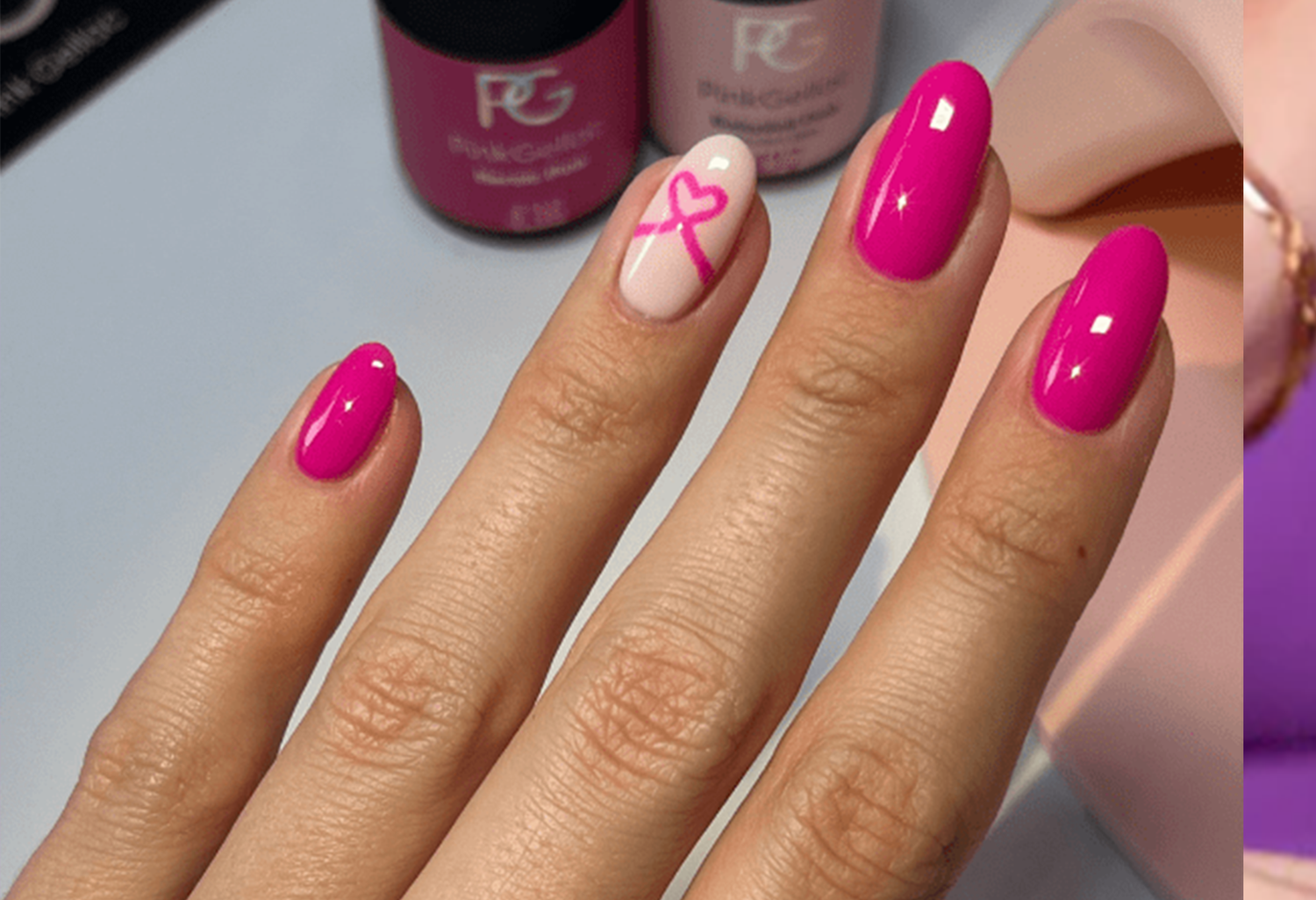 Pink painted nails, one with a pink ribbon on a white background; nail polish bottles in the background.