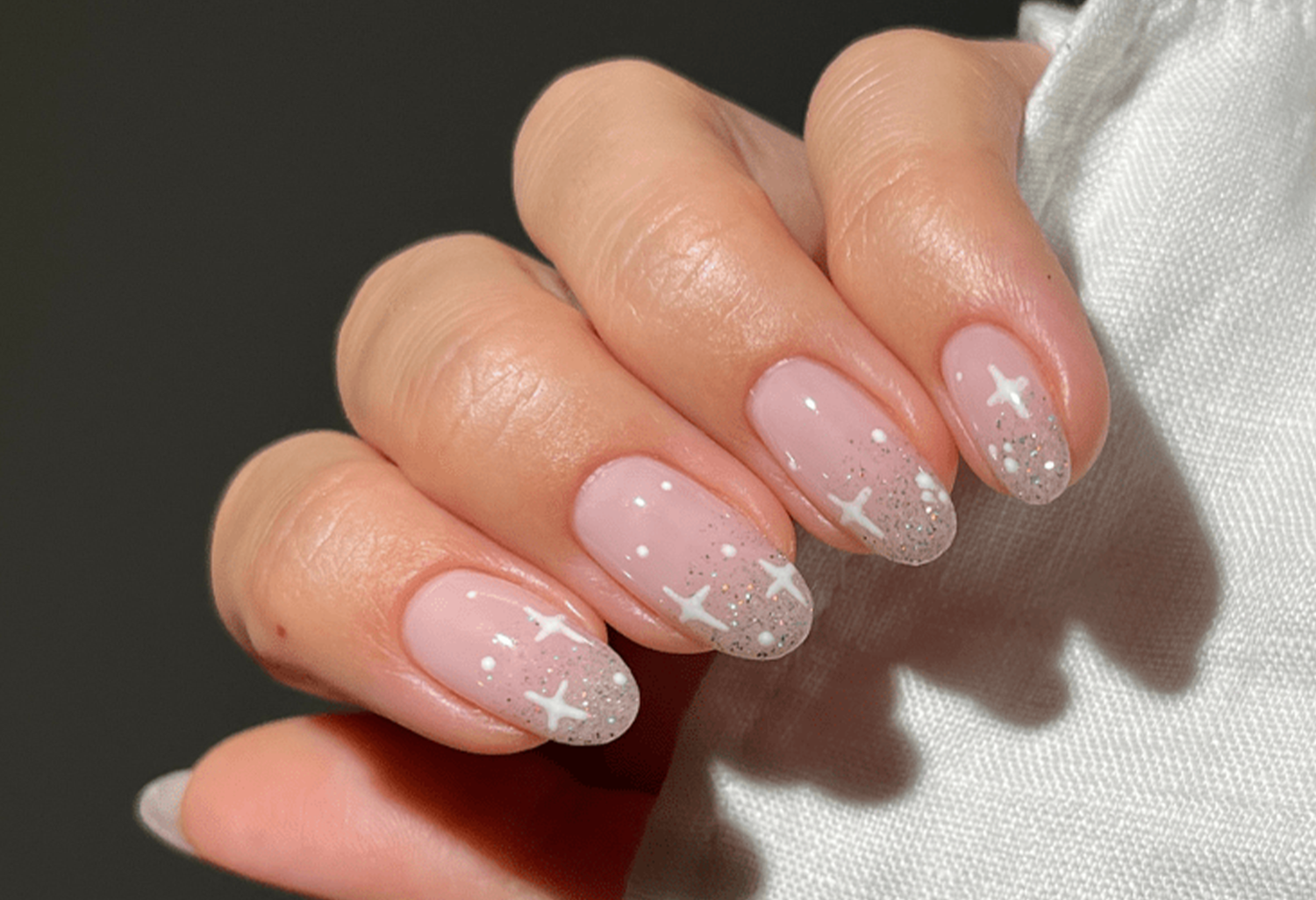 Close-up of a hand with pale pink nails decorated with white stars and silver glitters.