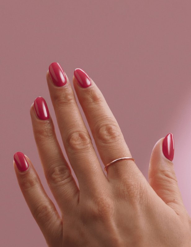 A hand with pink painted nails and a thin ring against a pink background.