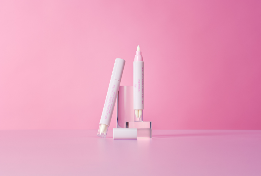 Two pink cosmetic pens on a pink background, one©©of which stands upright and the other leans at an angle, with a cap removed placed in front of it.