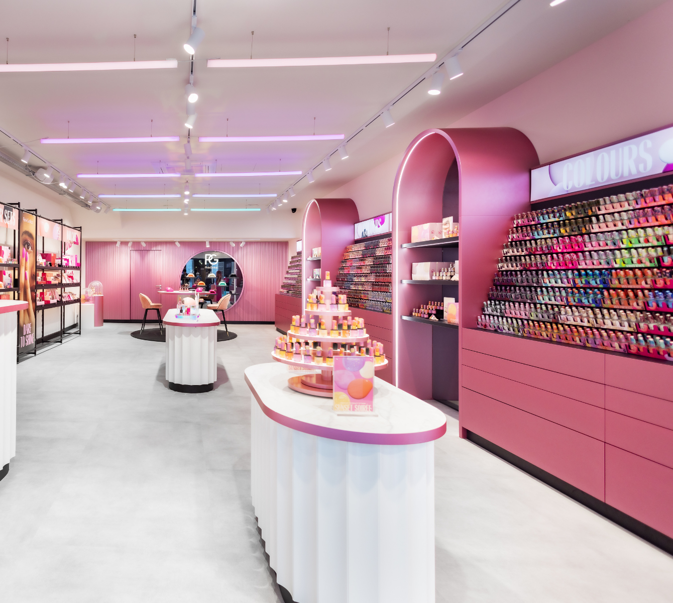 Stylish shop fittings with pink tones, exhibition racks full of colourful nail polishes and round tables with cosmetic products.