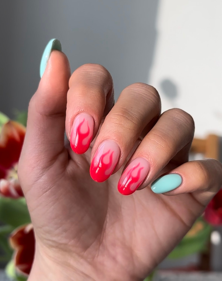 Hand with nails in green and pink tones, decorated with red flames.
