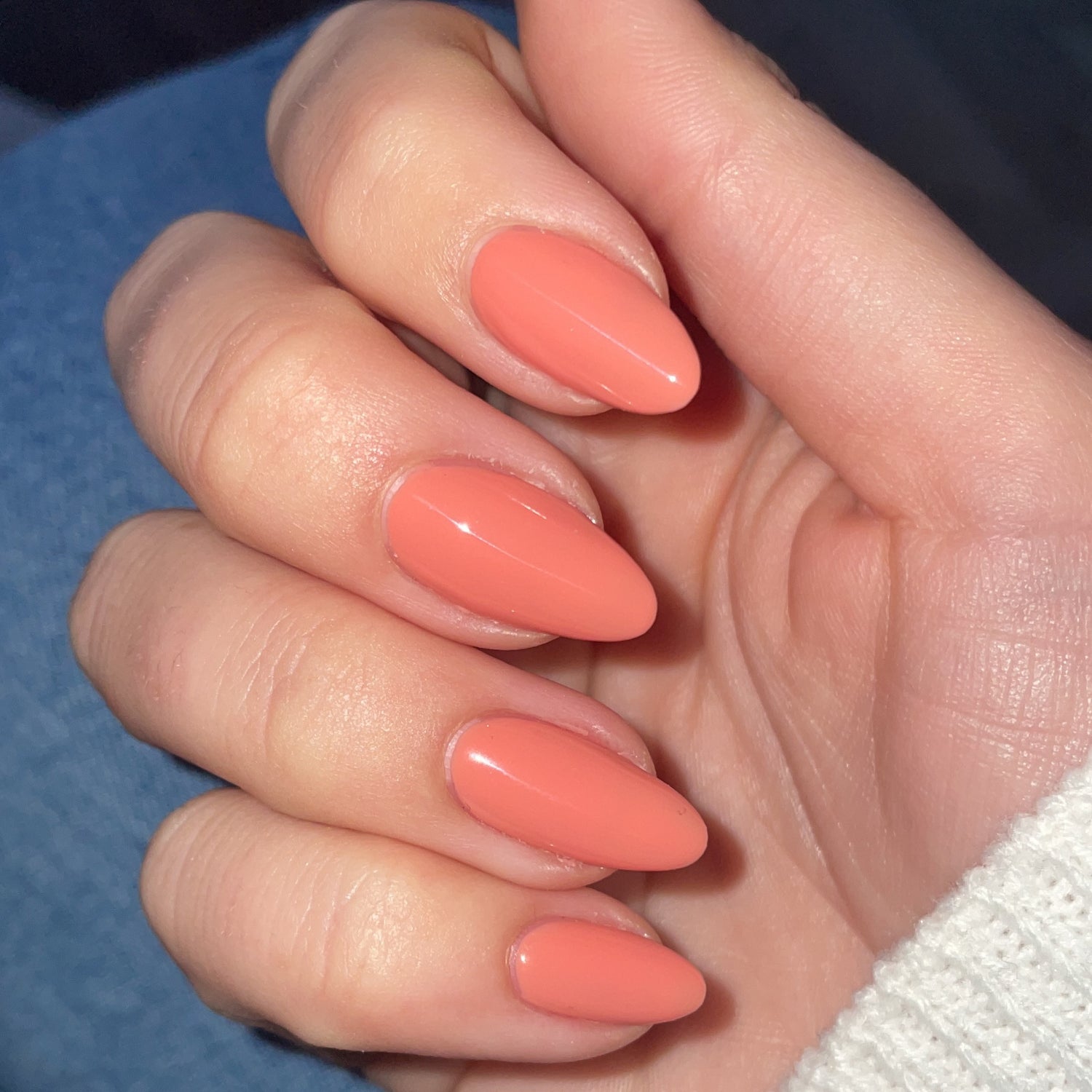 A hand with long, almond-shaped nails painted in a salmon pink color.