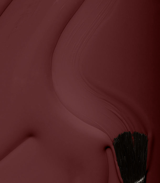 A brush strokes red paint over a surface, creating a smooth texture.