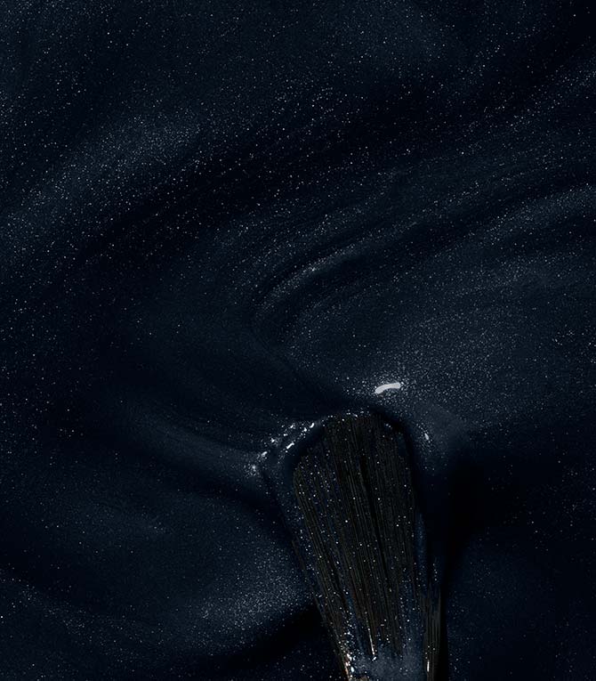 Close-up of a brush being drawn through a dark, shiny and shimmering substance.