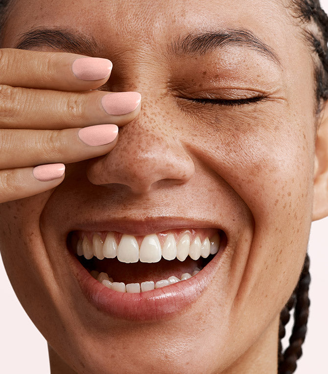 Close-up of a person with a hand covering one eye, showing a smile.
