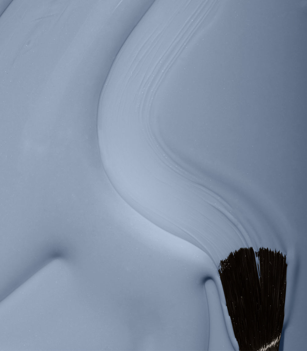 A brush sweeps light blue paint over a surface, with visible brushstrokes.