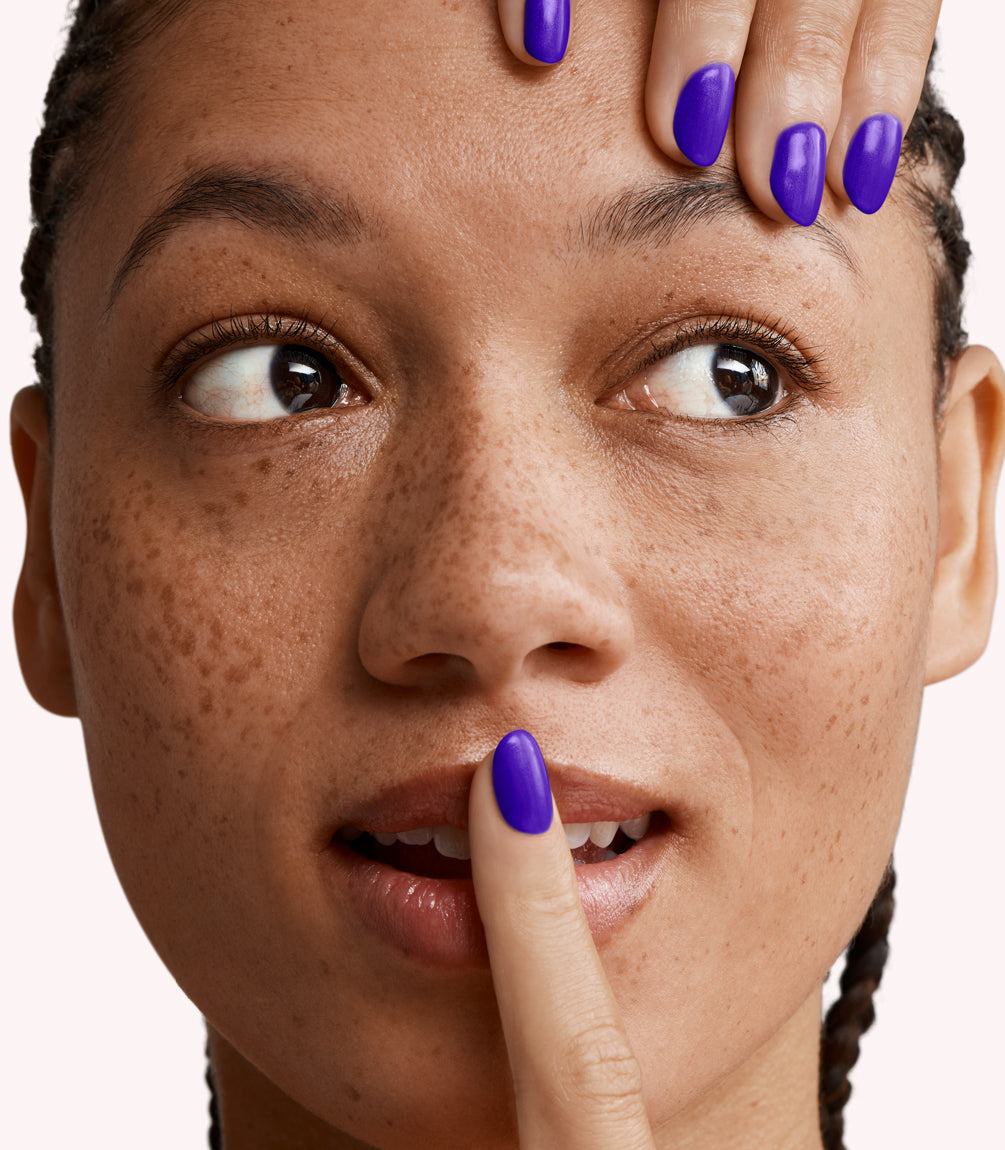 One person looks to the left while a hand with bright purple nails touches the forehead and another finger covers the lips.