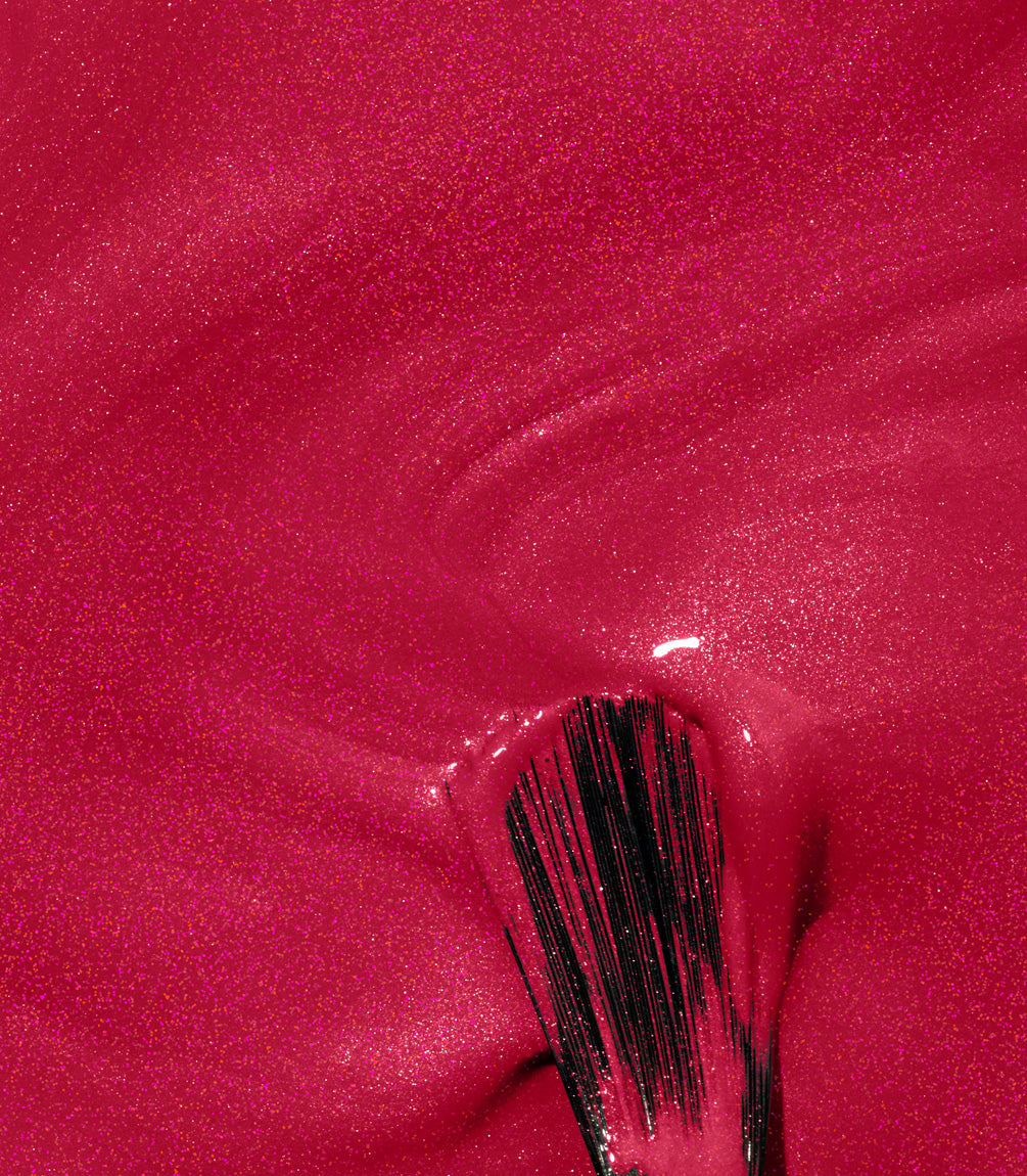 A close-up of a pink nail polish layer applied with a brush, with visible shimmering particles.
