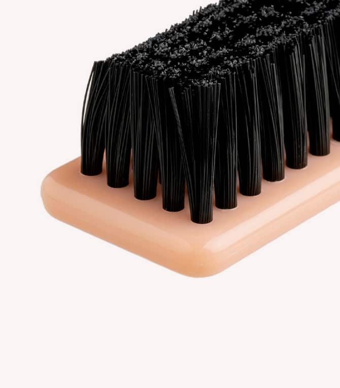 A shoe brush with a beige handle and black bristles.
