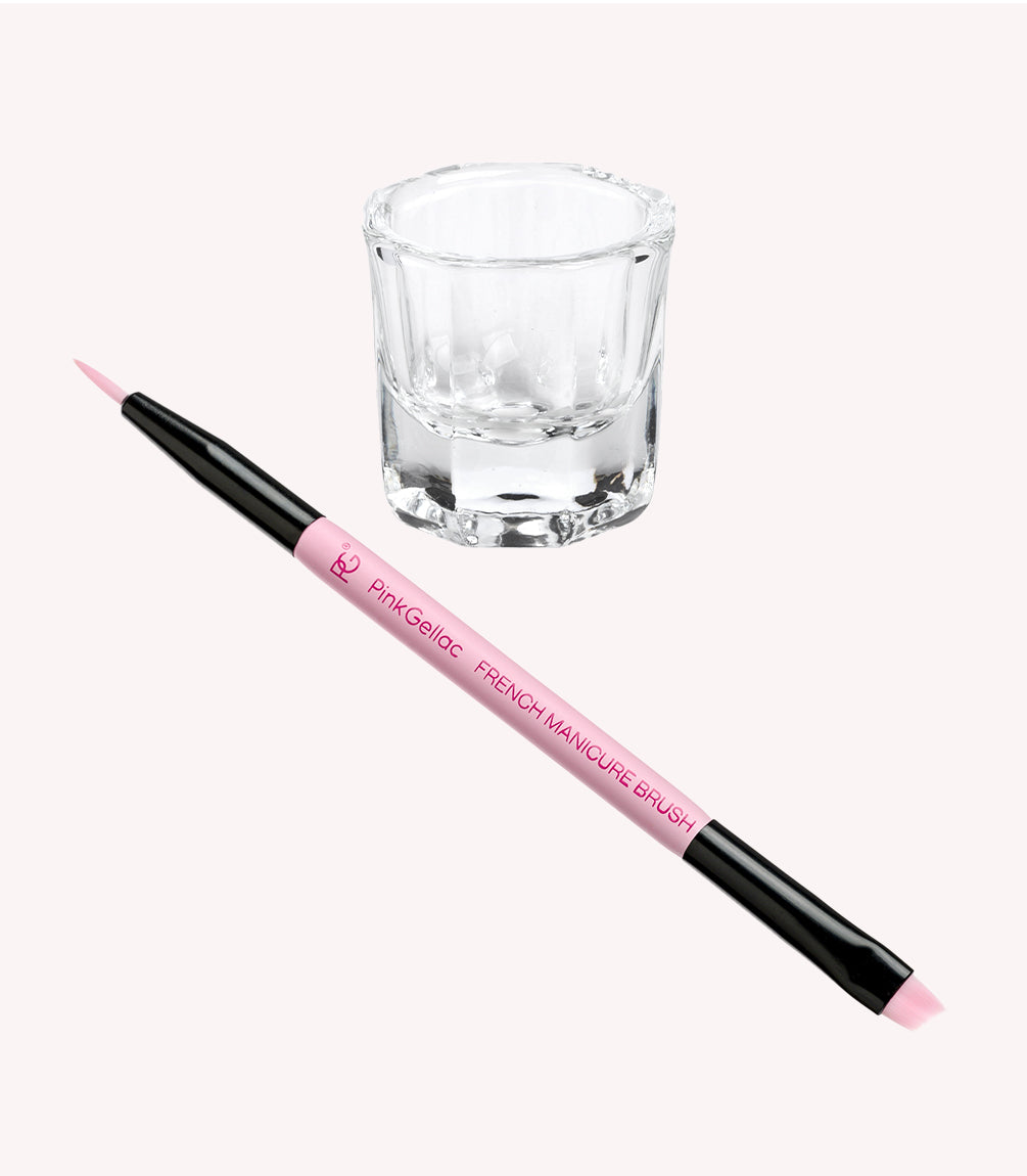 A pink French manicure brush and an empty glass cup on a light background.