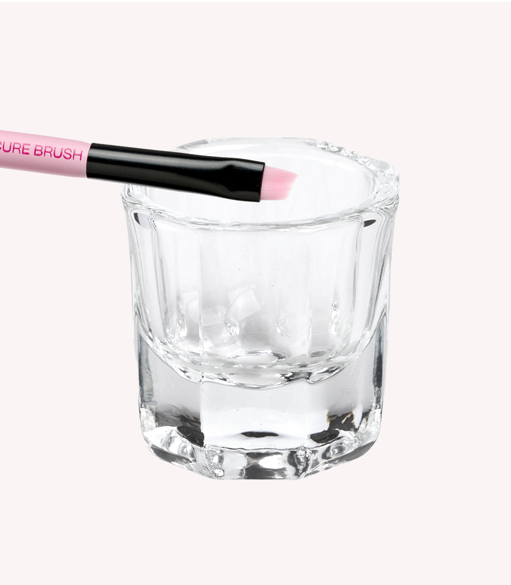 A glass jar with relief, in which rests a brush with pink and black details.