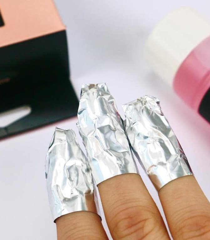 Three fingers covered with aluminum foil, with various cosmetic products in the background.