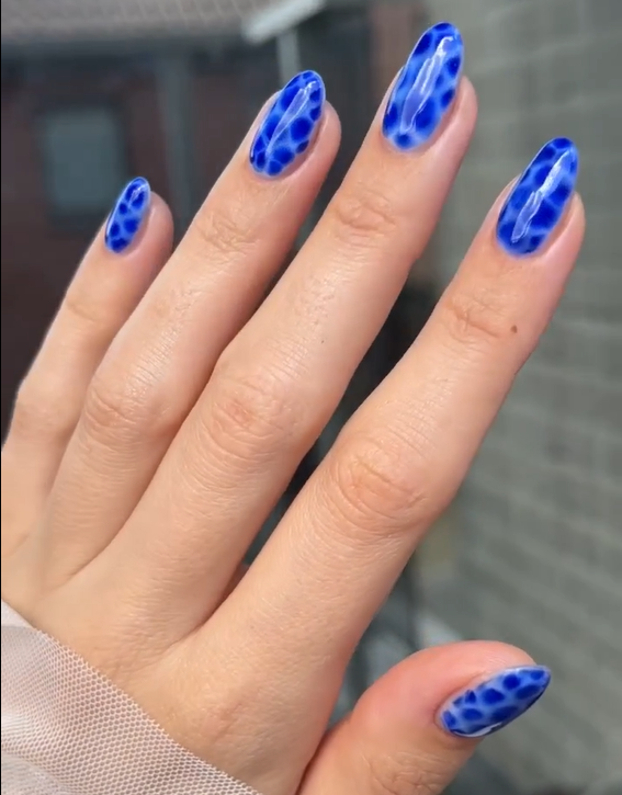 Close-up of a hand with bright blue nails with a white marble-like pattern.