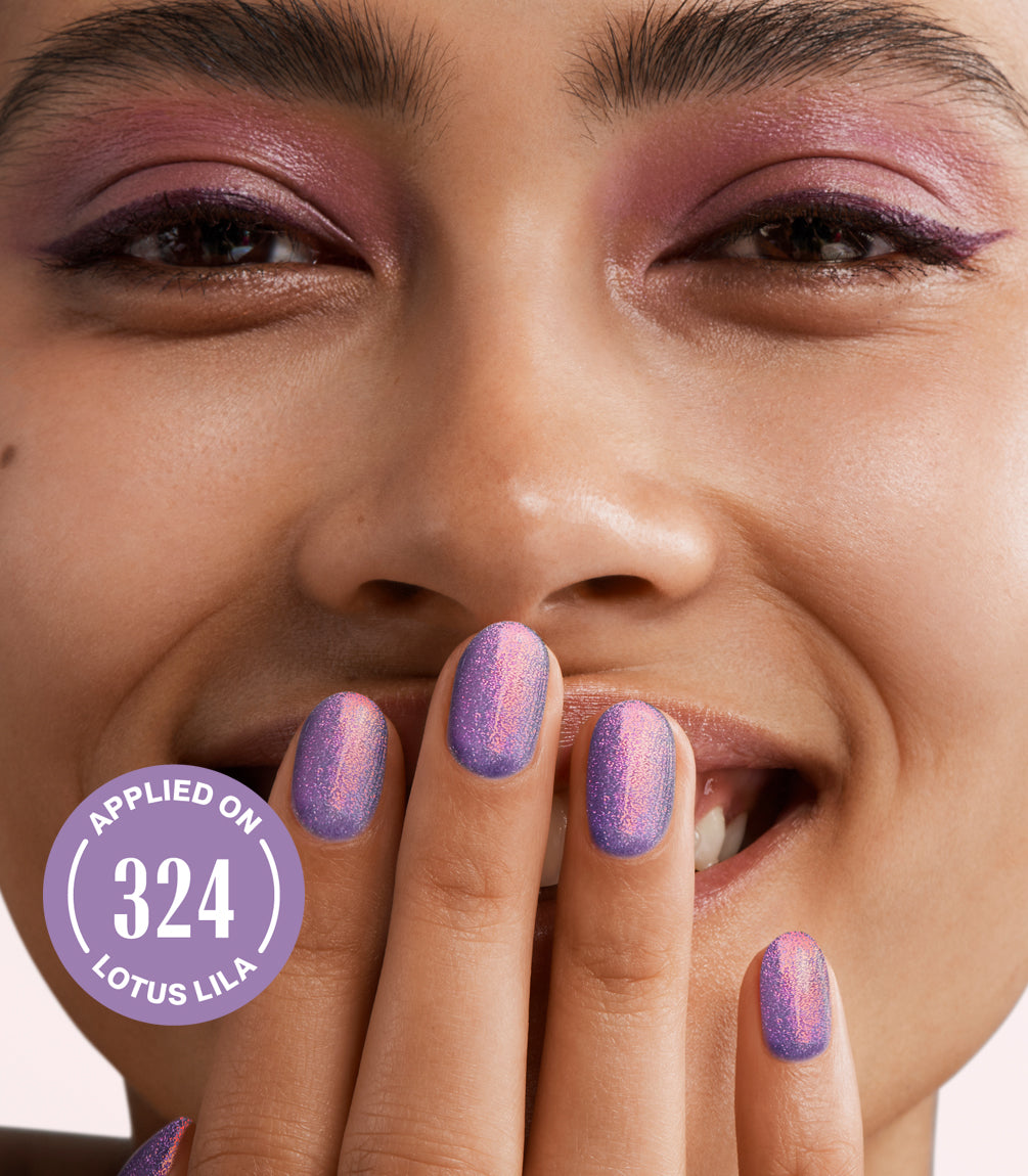 Close-up of a smiling person wearing purple eyeshadow and shiny purple nail polish, with the text "Applied on 324 Lotus Lilac" in a circle depicted in the image.
