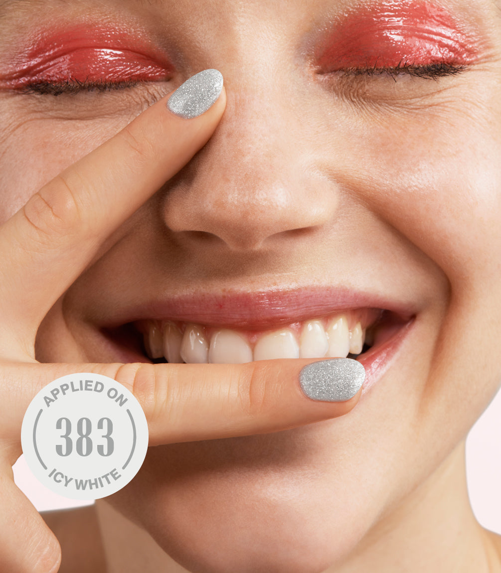 Person with powdered red eyeshadow, smiling and pointing to face with silver glitter nail polish; text "Applied on 383 Icy White" visible.