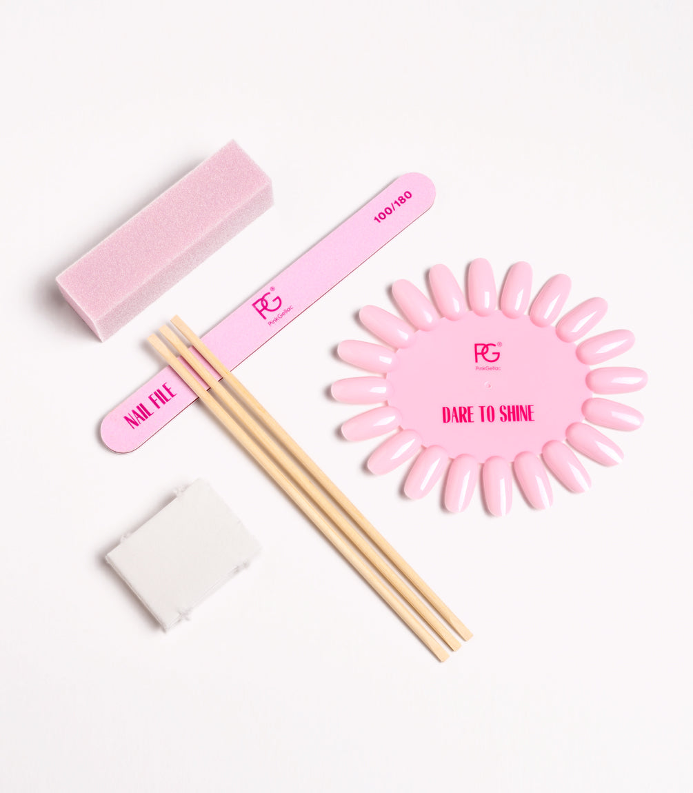 Nail art tools on a white background, including a pink nail file, polishing block, wooden sticks, display with pink artificial nails and a cloth.