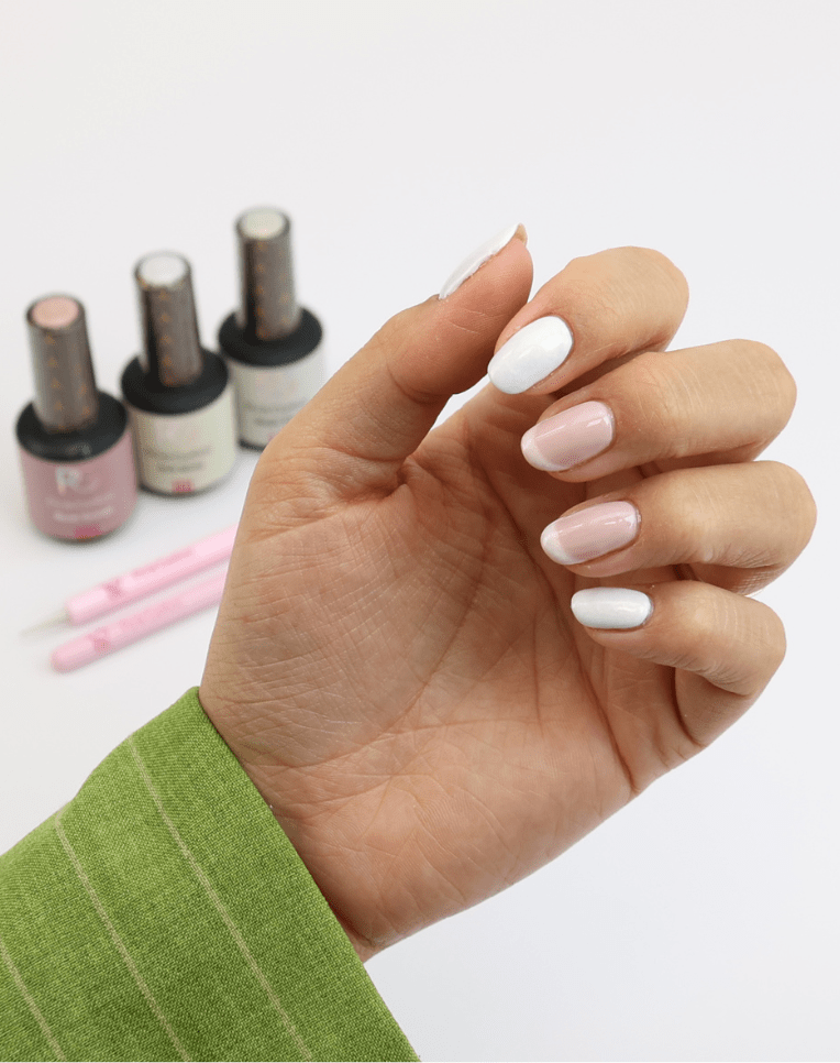Hand with modern nail design in pink and white, green sleeve and nail polish bottles and brushes in the background.