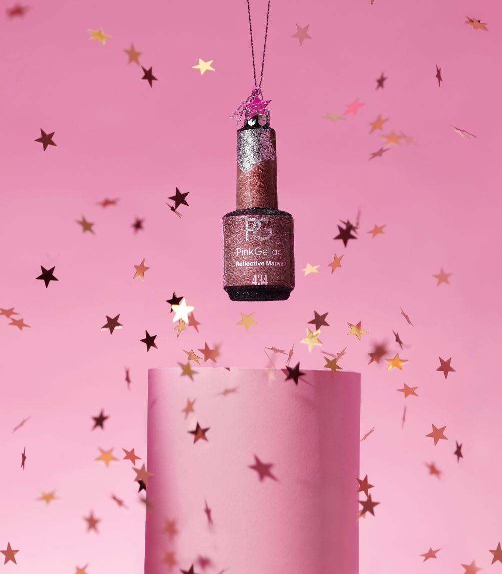 Bottle of nail polish hangs on a thread against a pink background, surrounded by glittering star-shaped confetti.