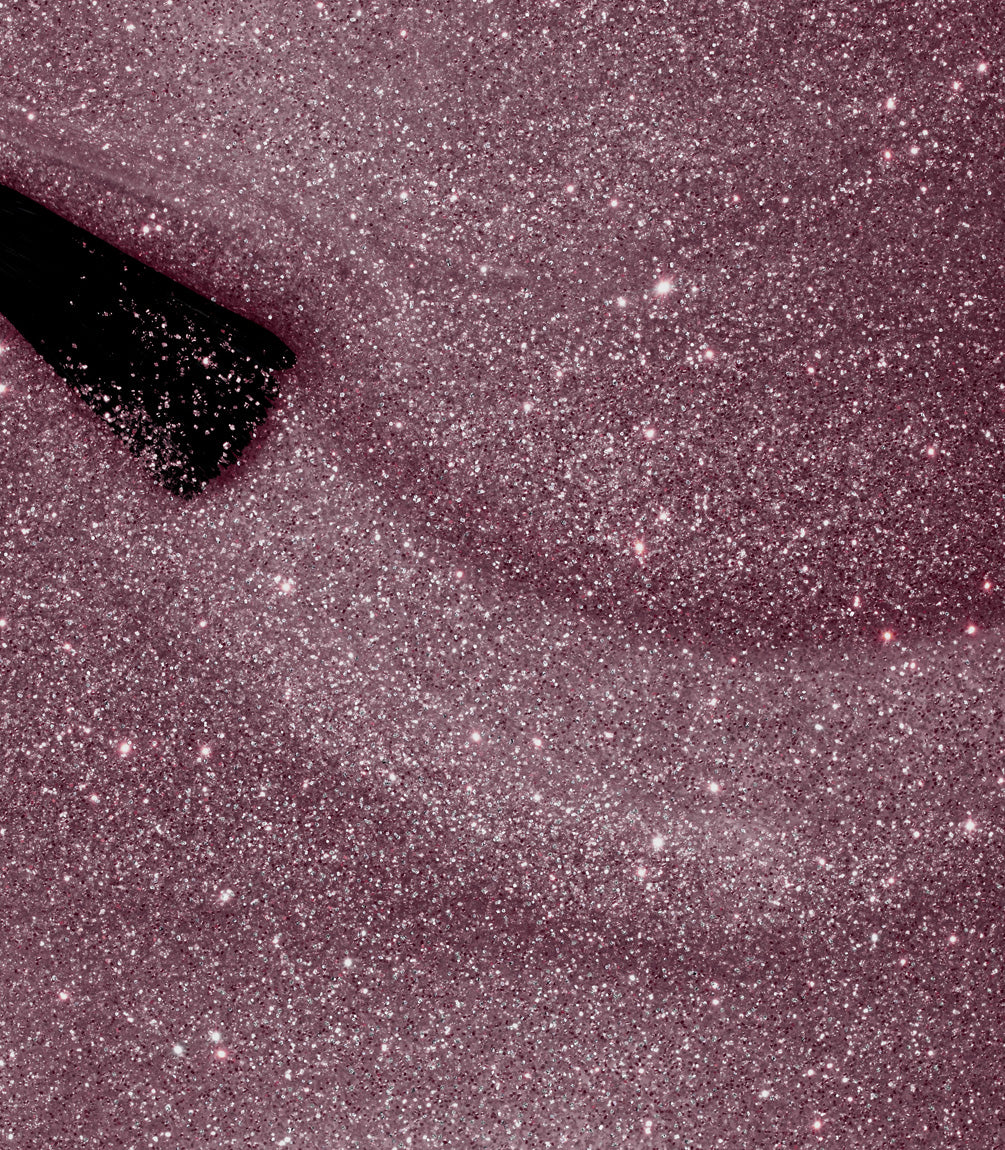 A makeup brush glides through pink glitter powder, creating a shimmering trail.