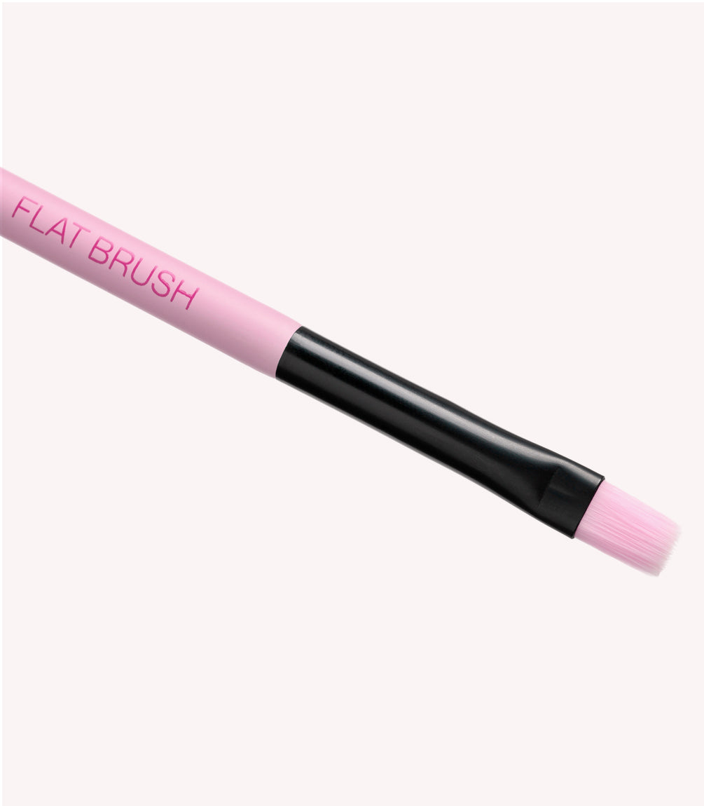 Pink makeup brush with black handle and flat bristles, on a light background.