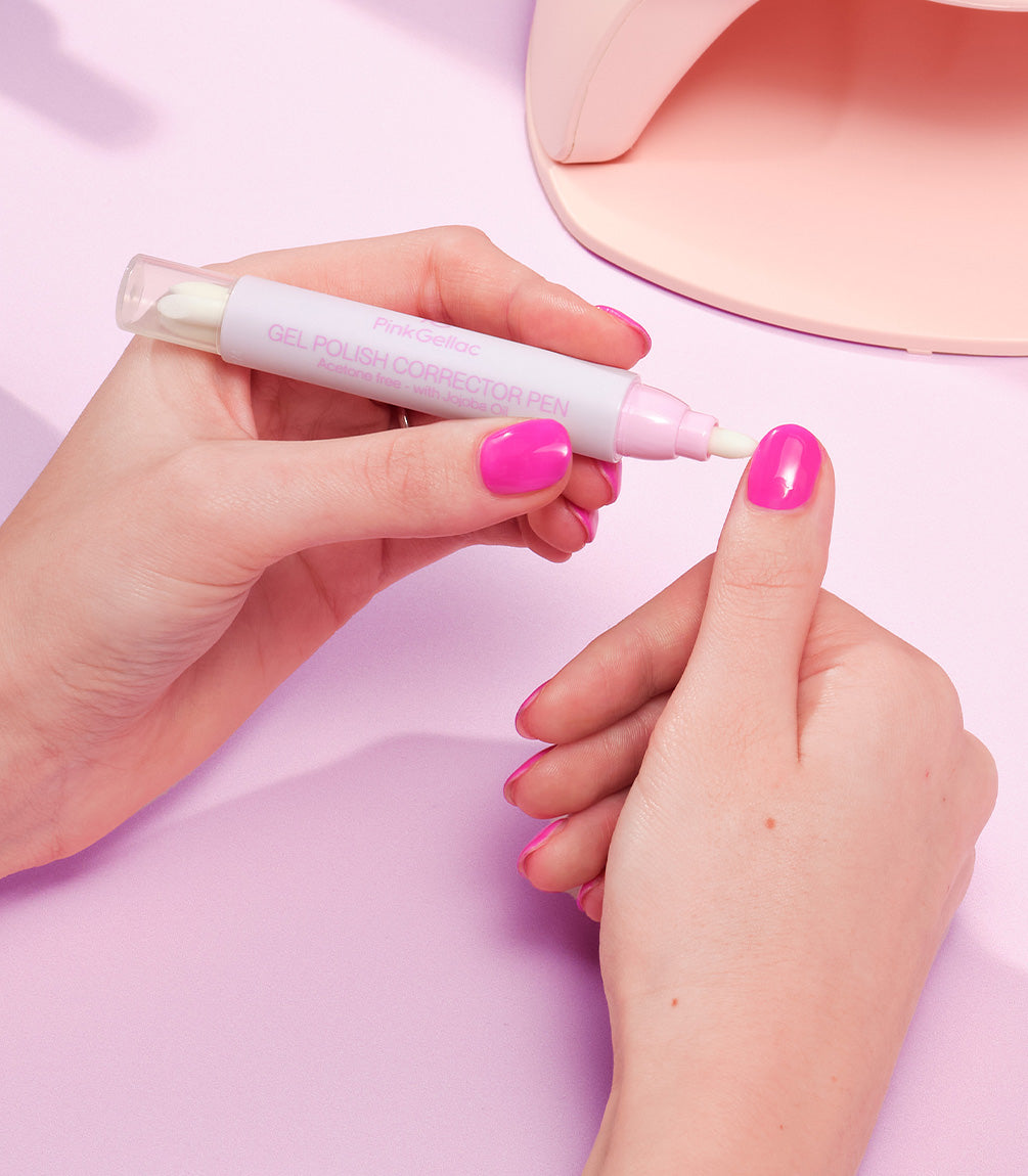 A person uses a nail polish corrector pen to correct pink nail polish on the nails.