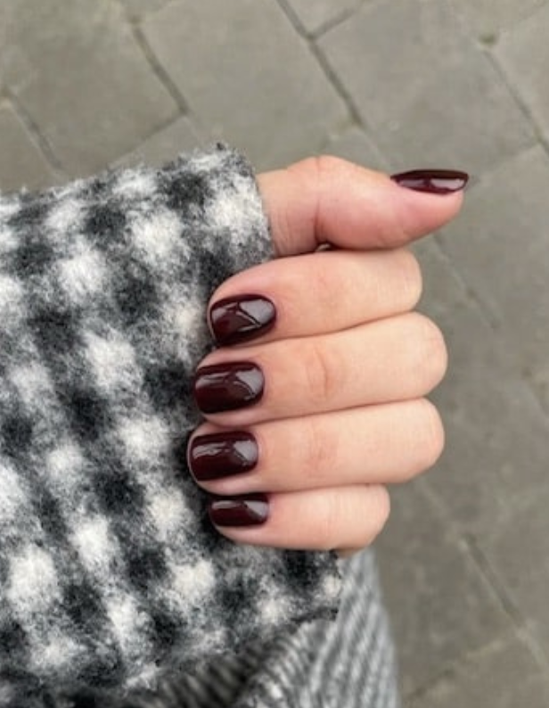 Hand with short-cut nails painted in a burgundy color, set in a black and white checkered fabric, with a stone background.