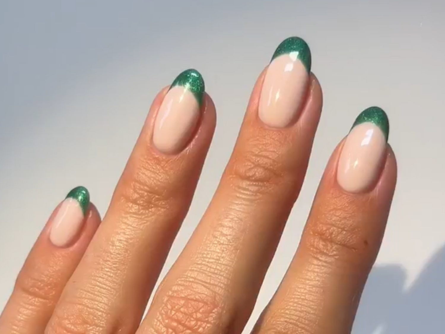 Three fingers with almond-shaped nails, lacquered in nude color with a green shimmering tip.