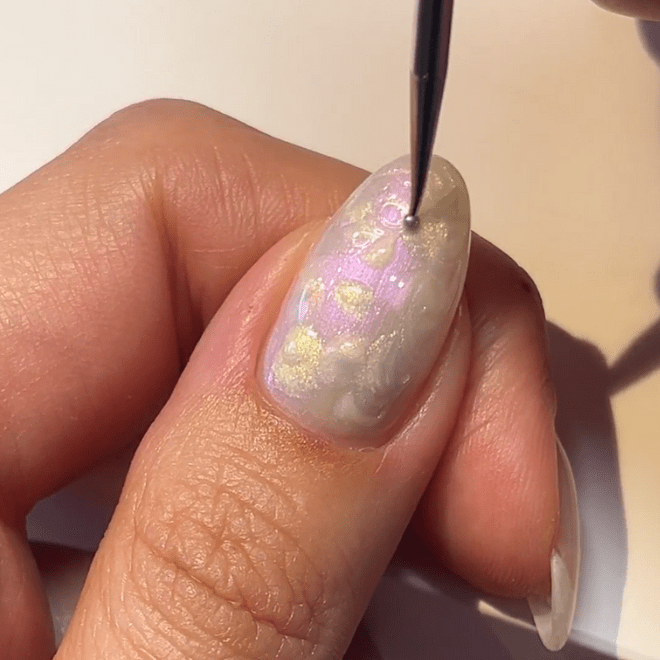 Hand holding nail in mother-of-pearl color pattern, decorated with a brush.