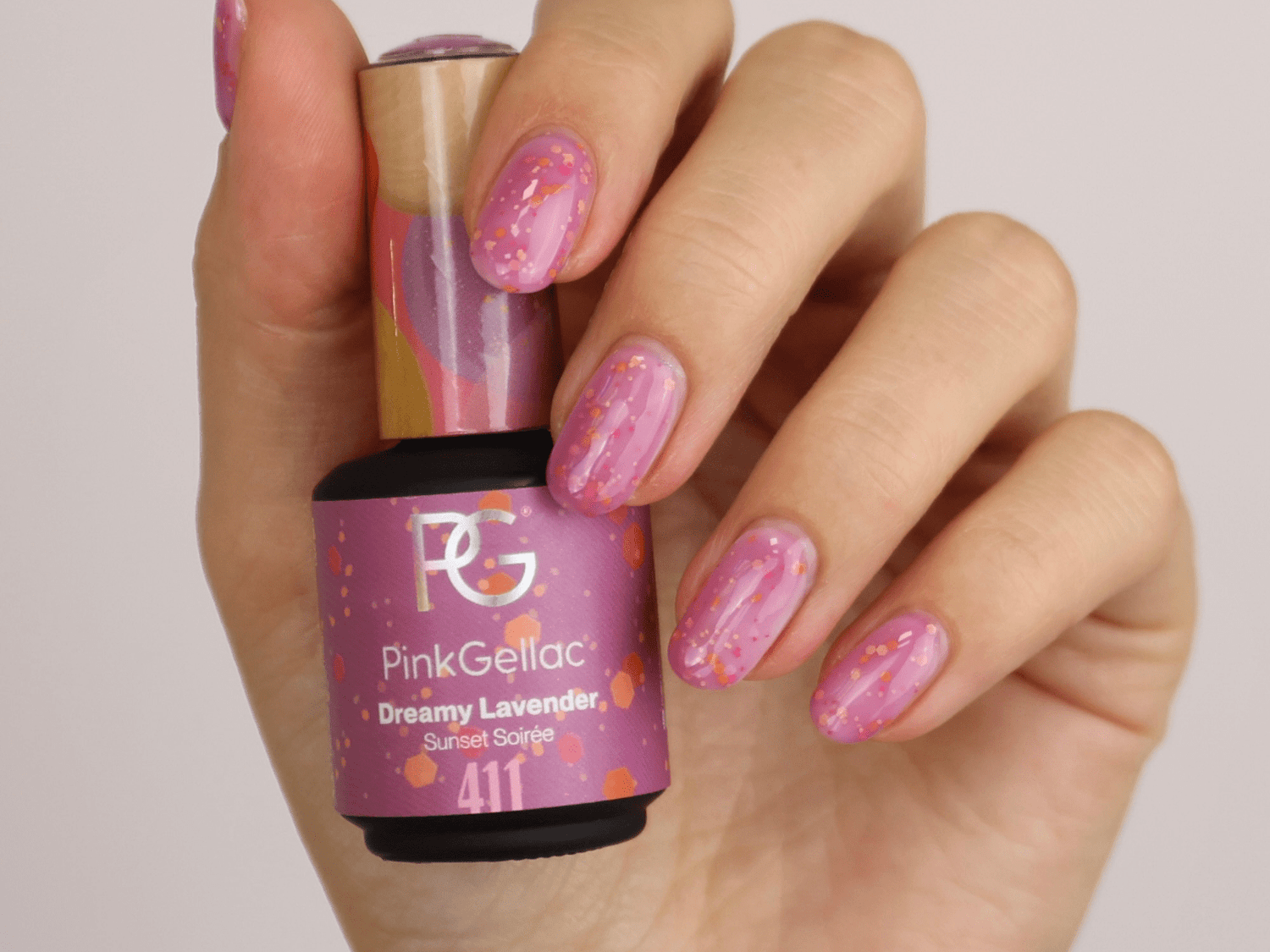 A hand with painted nails in purple shades with glitter, holding a bottle of purple nail polish.