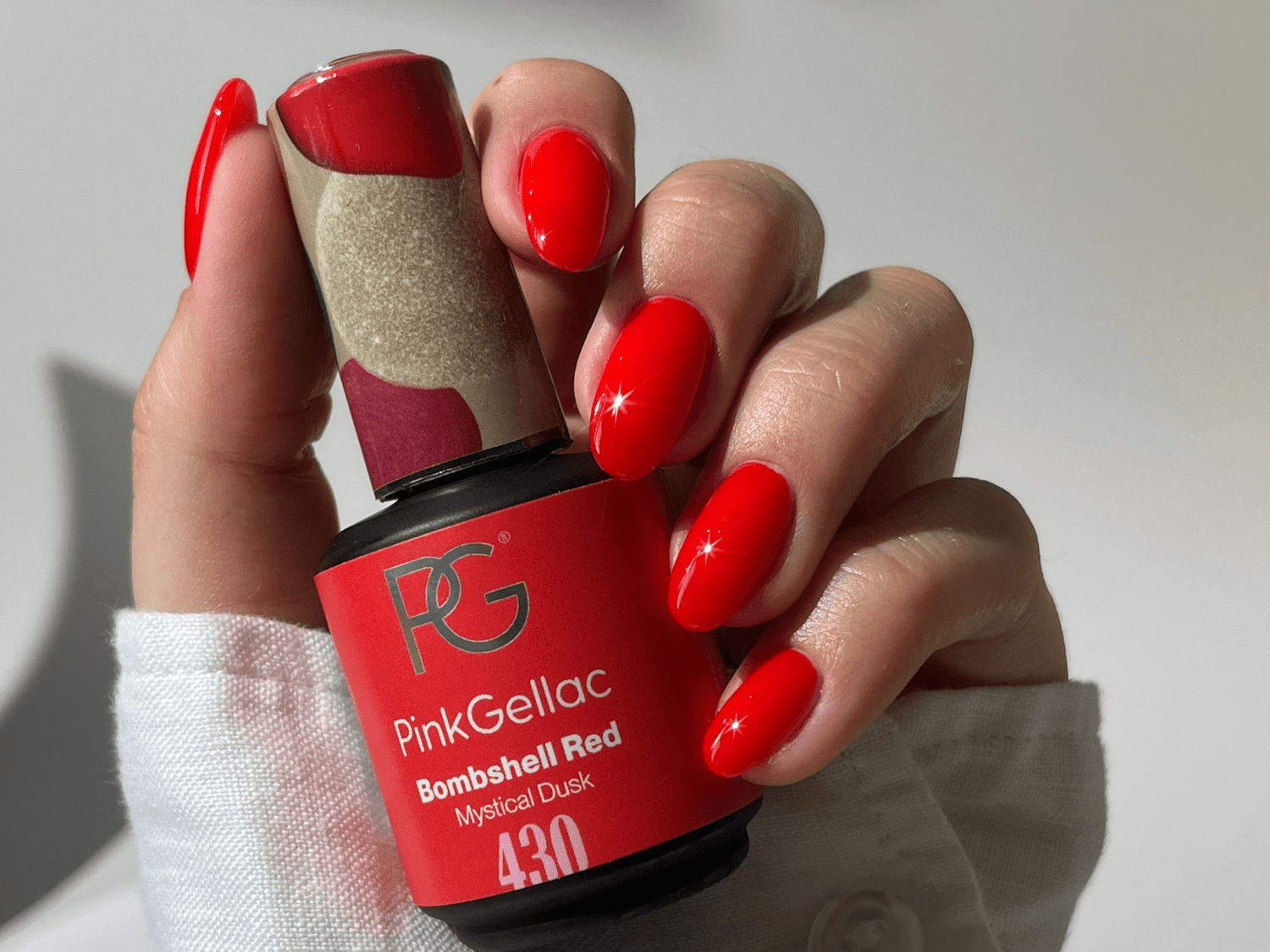 Red nail polish bottle with made-up nails, against a neutral background.