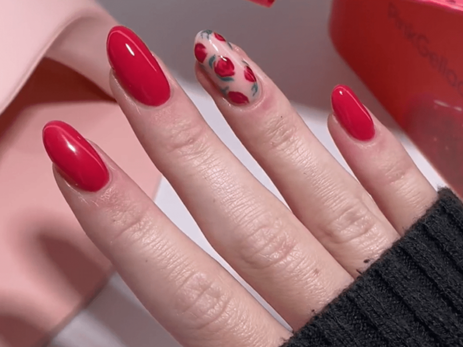 Hand with nails provided with red nail polish, with the ring finger having a design with red flower accents.