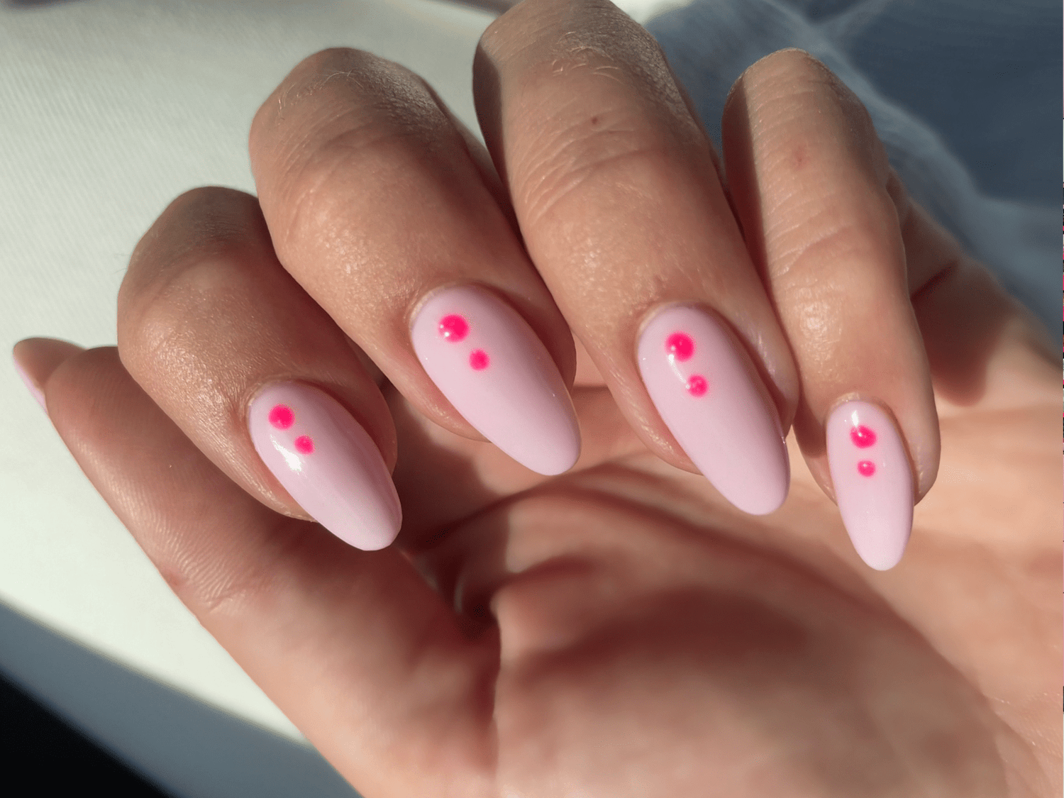 Close-up of a hand with pale pink nails decorated with small pink dots.
