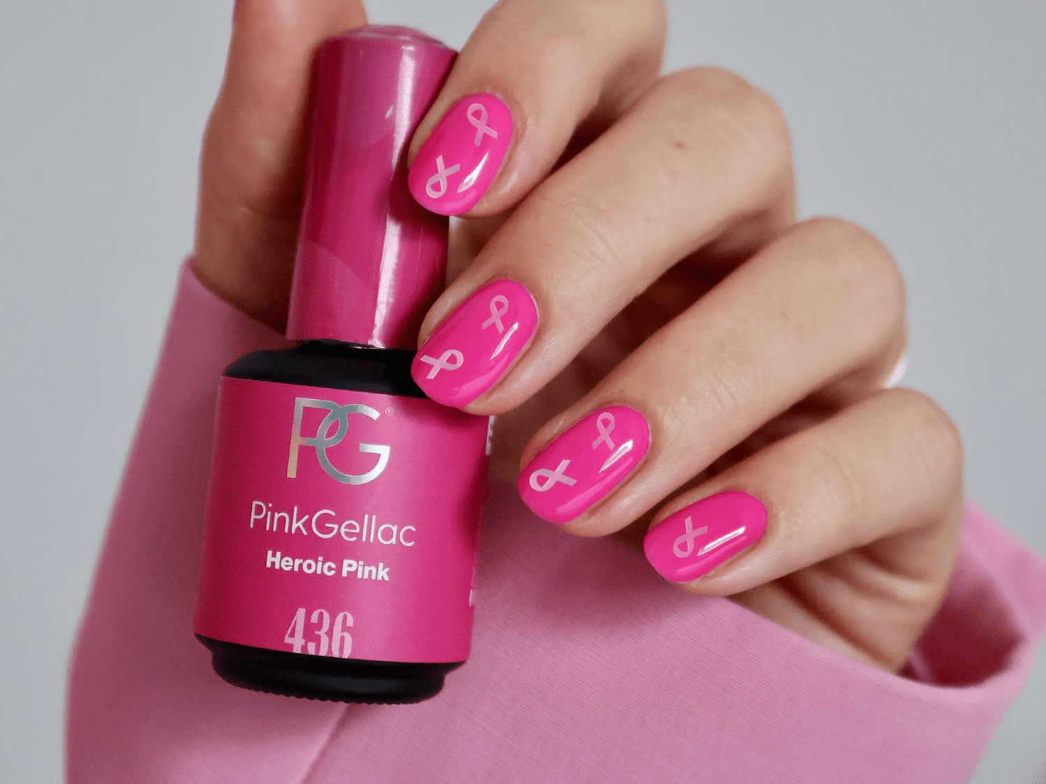 Hand with pink nail polish and white ribbons, holding a Pink Gellac bottle.
