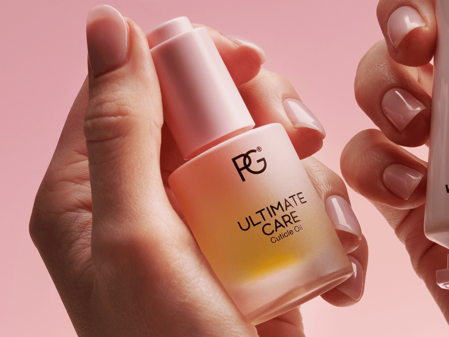 Hands holding a bottle of cuticle oil with pink background.