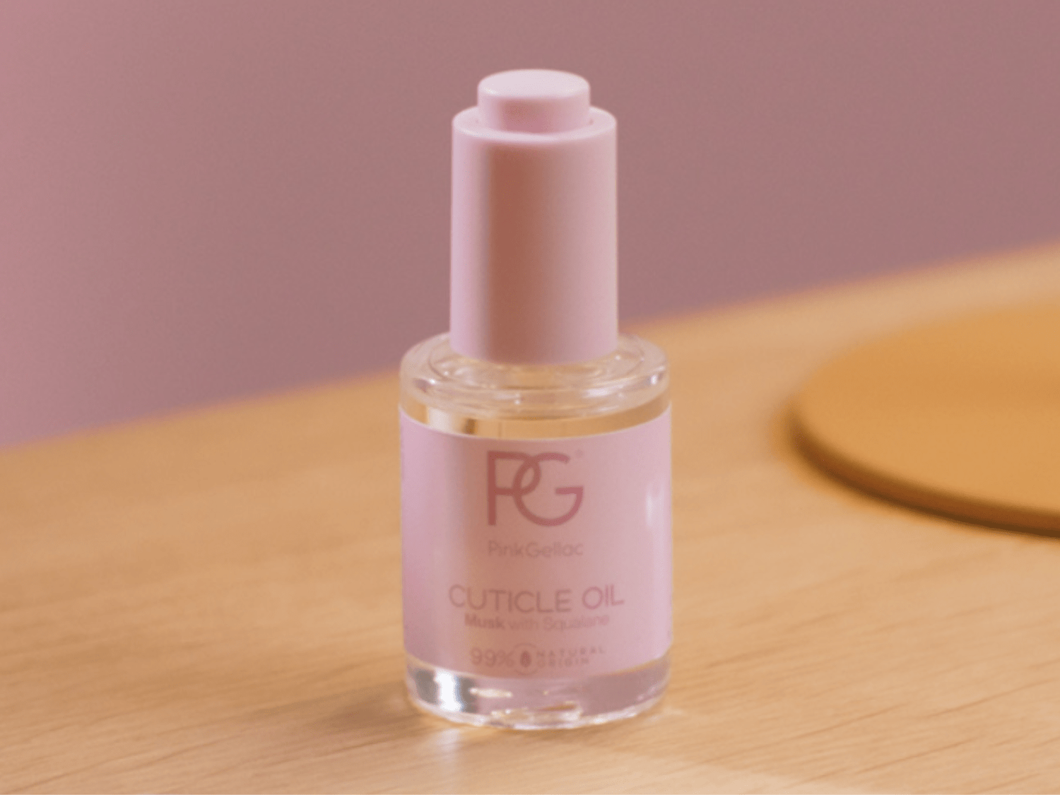 Pink bottle of cuticle oil on wooden surface, with round cap and brand name. Suggested for nail care.