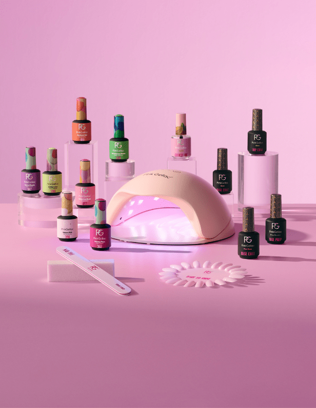 Alt: A collection of nail care products, including several nail polish bottles, a UV lamp, a file, and other manicure supplies, all presented on a pink background.