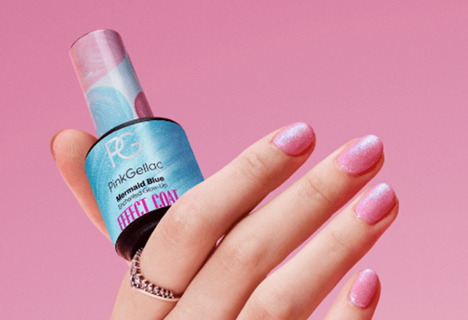 Hand with pink glitter nail polish and a bottle of blue Pink Gellac, against a pink background.