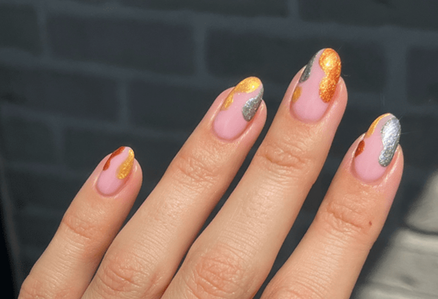 Hand with pink nails, decorated with gold and silver in an abstract pattern.