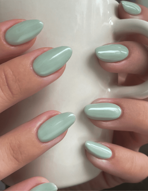 Green manicured nails holding a white mug.