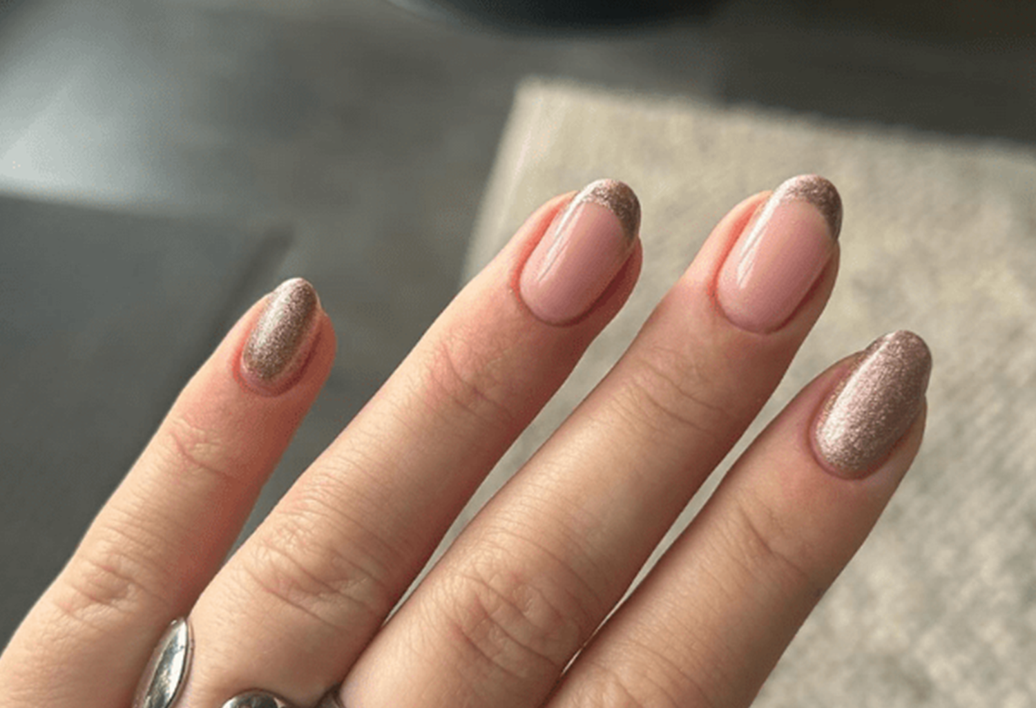 A hand with nails in a blush pink color and shimmering brown-gold tips, against a neutral background.