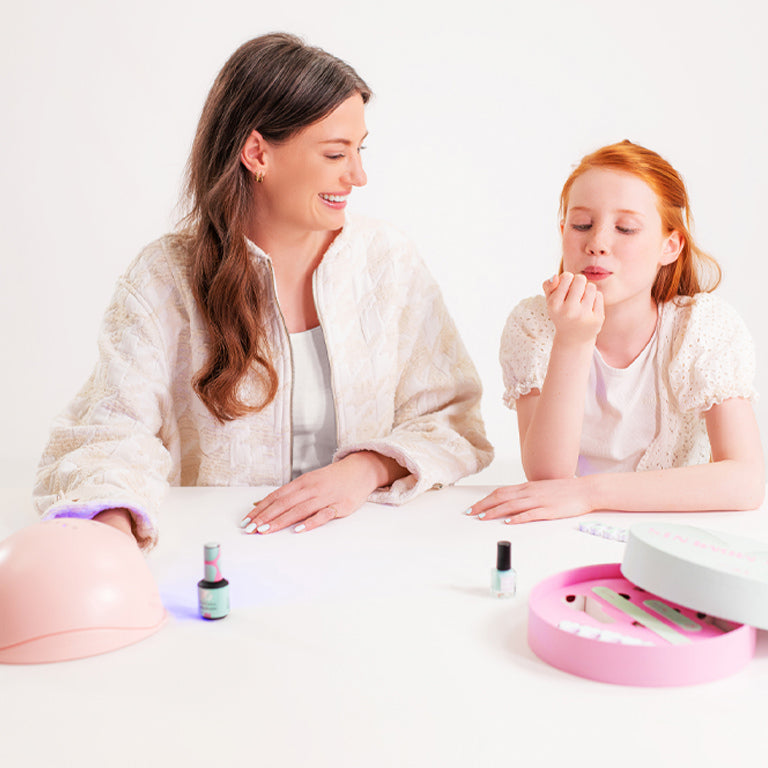 Woman and girl do a manicure together with nail polish and a UV lamp on a white table.