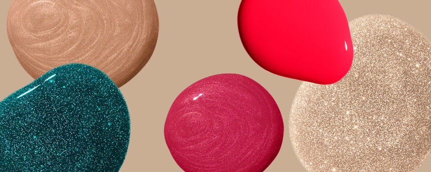 Different colored nail polish drops on a beige background, including shimmering gold, bright red, pink, green and neutral shades.