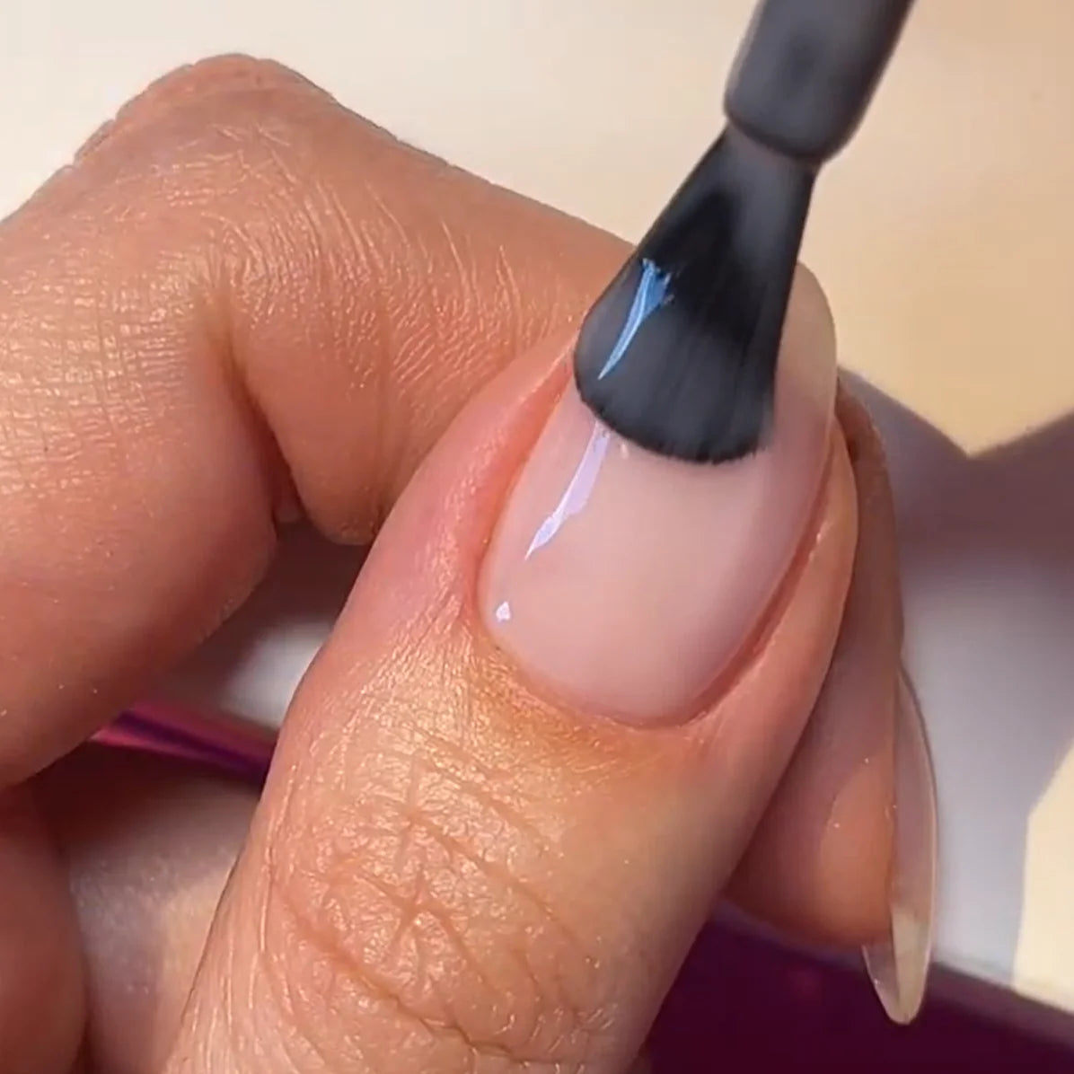 A close-up of a hand with a brush applying clear nail polish to a nail.